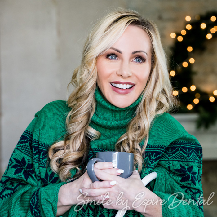 close up of smiling woman in green sweater holding a cup of tea