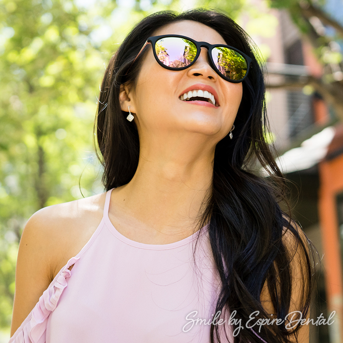 asian woman in sunglasses smiling and looking into the sun