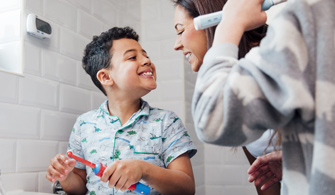 Children are brushing their teeth in the bathroom at home. The mother is checking the little boy's mouth to make sure he has brushed properly.