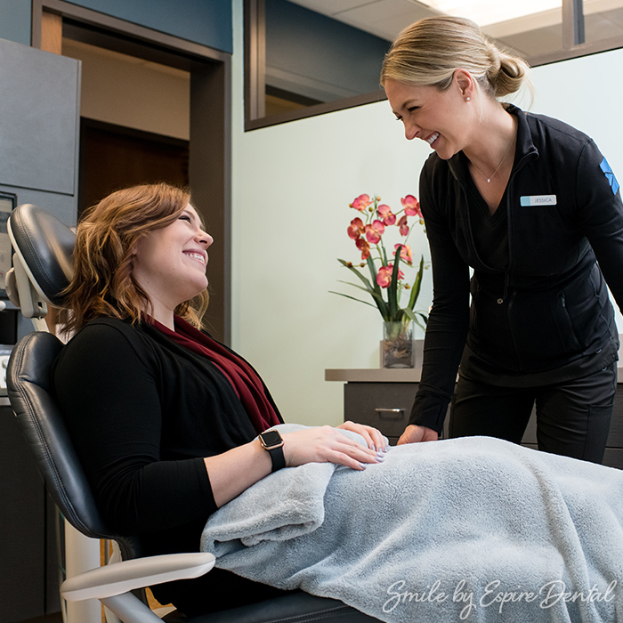smiling woman in dentist's chair talking to smiling female dental assistant
