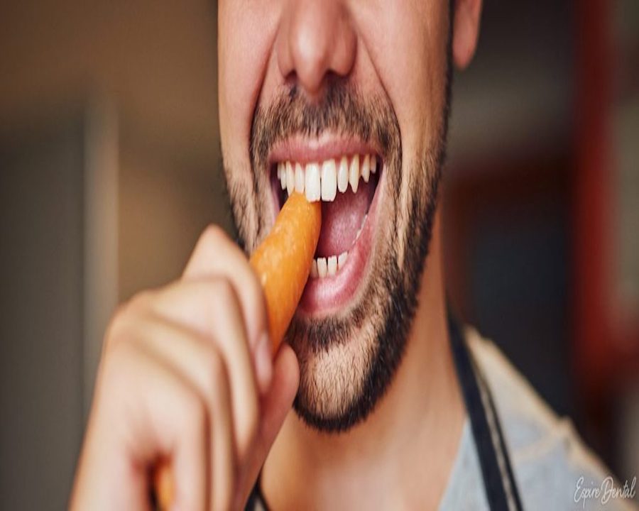 man with straight teeth biting into carrot