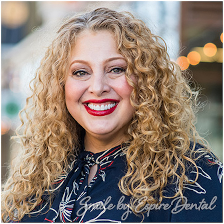white woman with curly hair smiling and wearing red lipstick
