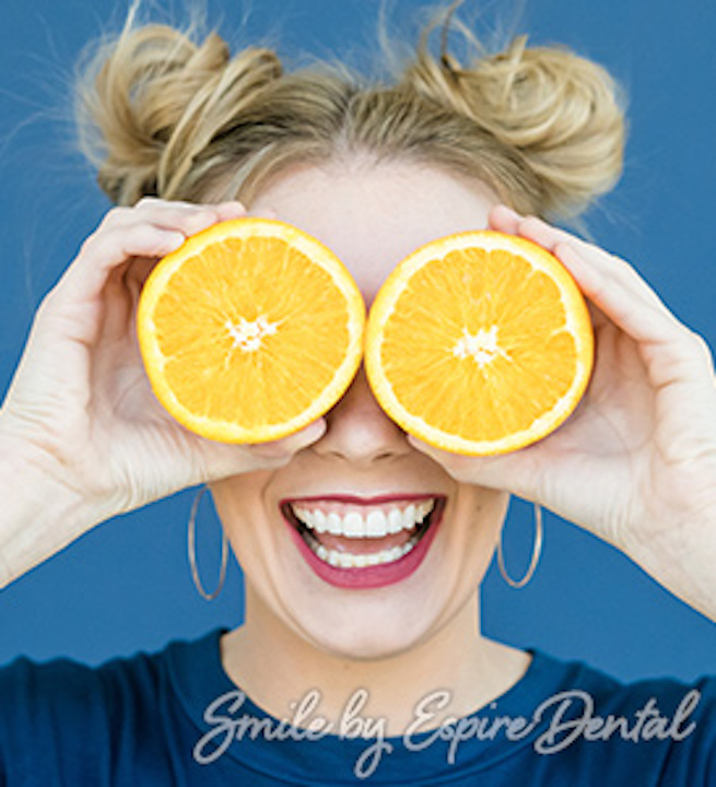 model smiling and holding oranges in front of her eyes