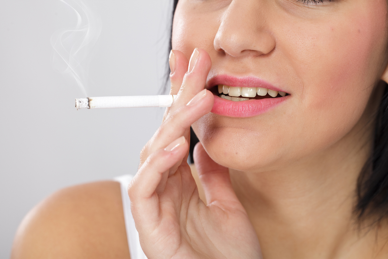 Close up of a young woman with bad skin and yellow teeth, smoking a cigarette